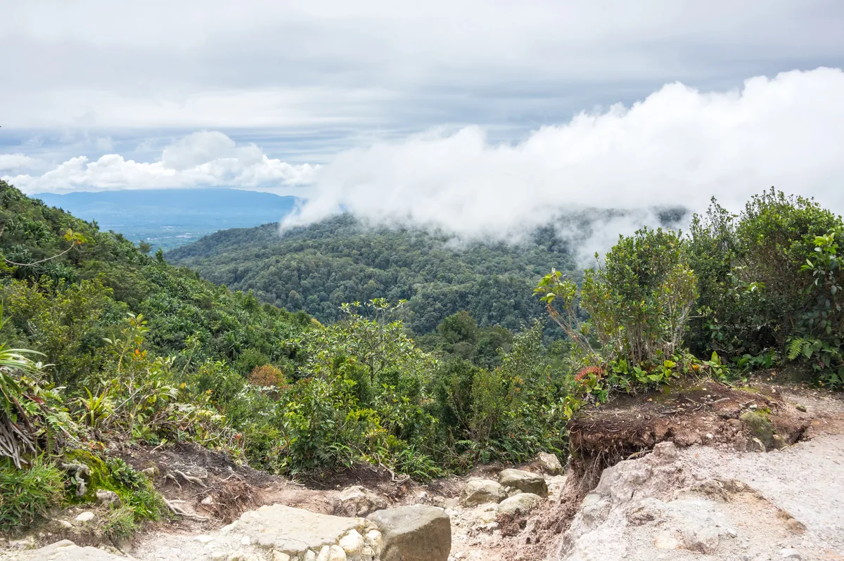 Rocky hiking trail on Mount Sibayak with forested hills beyond